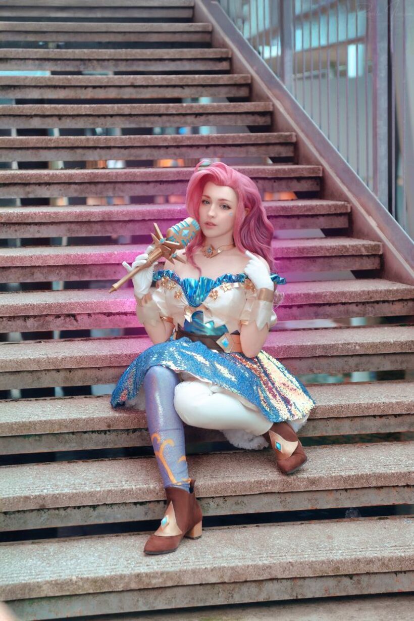 Cosplayer con parrucca rosa e abito scintillante seduta su una scalinata