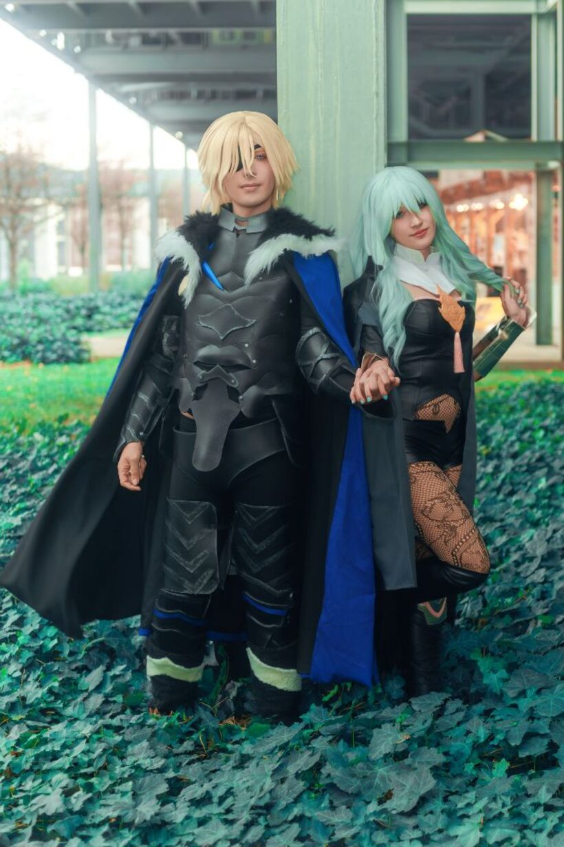 Due cosplayer in costume storico-fantasy che si tengono per mano su un tappeto di edera