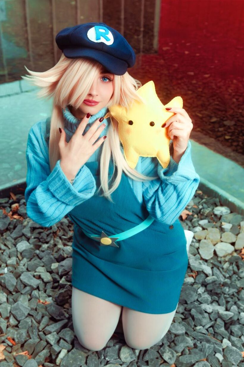 Cosplayer in costume blu inginocchiata su un letto di ghiaia con un peluche a forma di stella