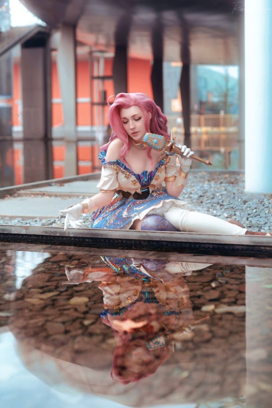 Cosplayer in costume scintillante seduta accanto a uno specchio d'acqua che ne riflette la figura